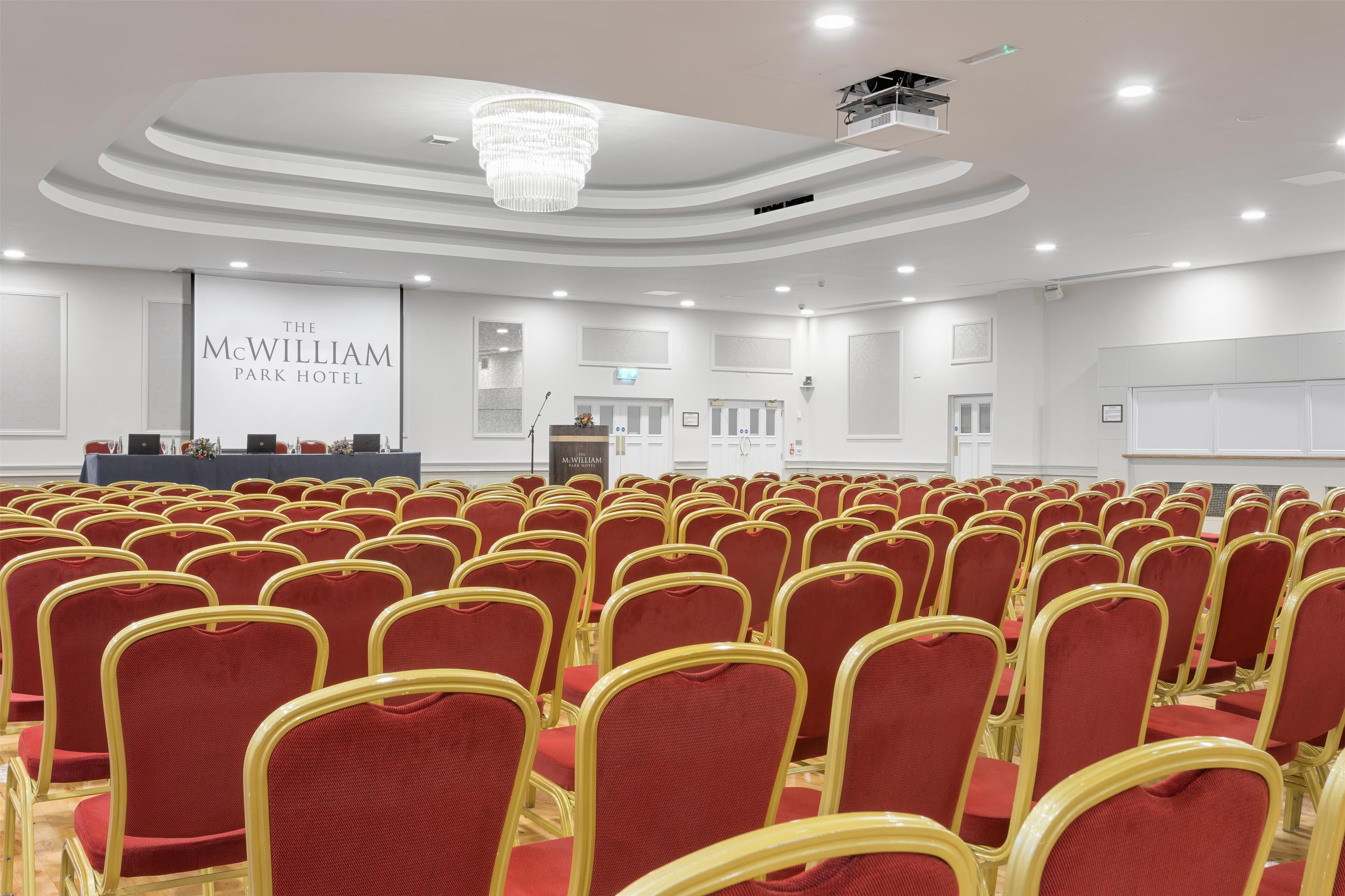 A conference room with rows of red chairs and a stage with a podium.
