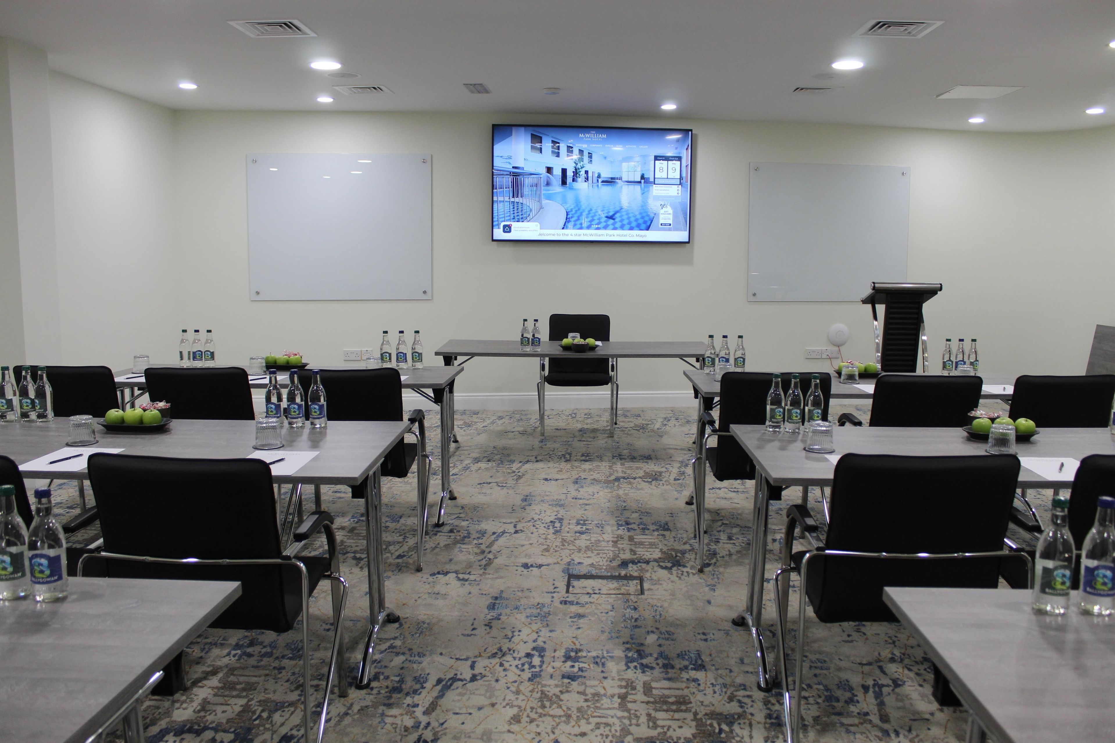 A conference room with tables, chairs, water bottles, and a projector screen displaying a presentation.