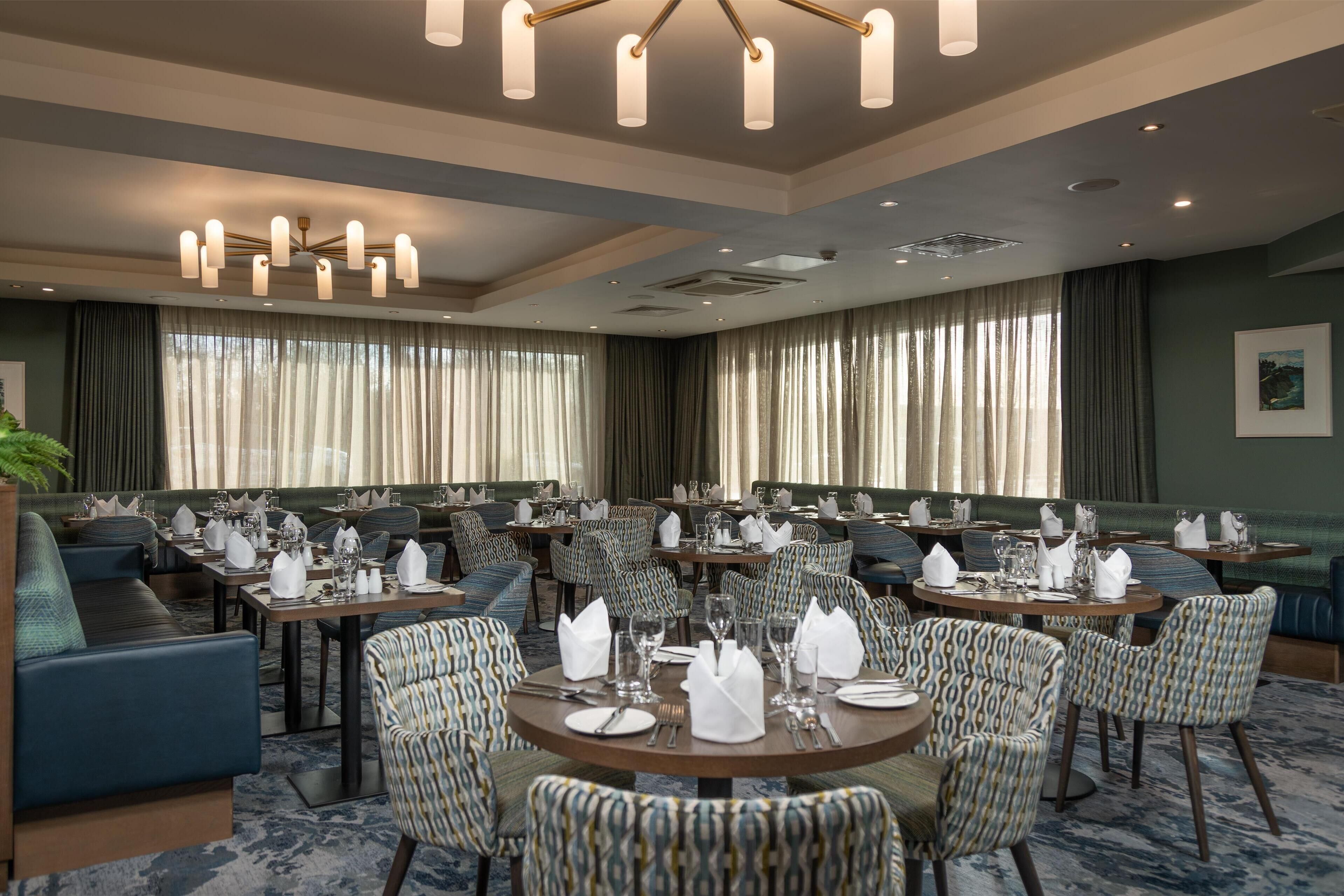 A hotel dining area with round tables, patterned chairs, and a chandelier.
