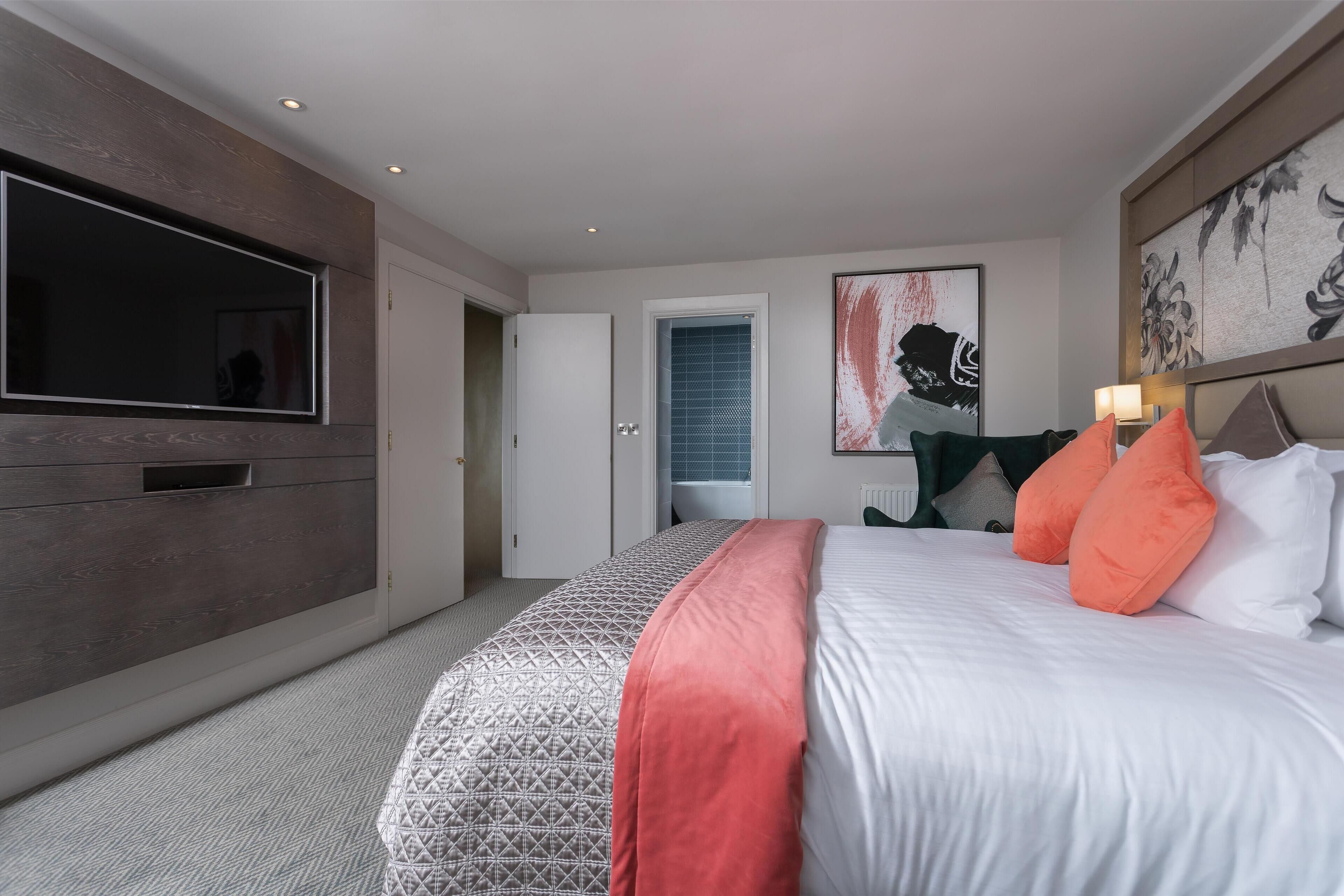 A modern hotel room with a large bed, a flat-screen TV, and artwork on the walls.