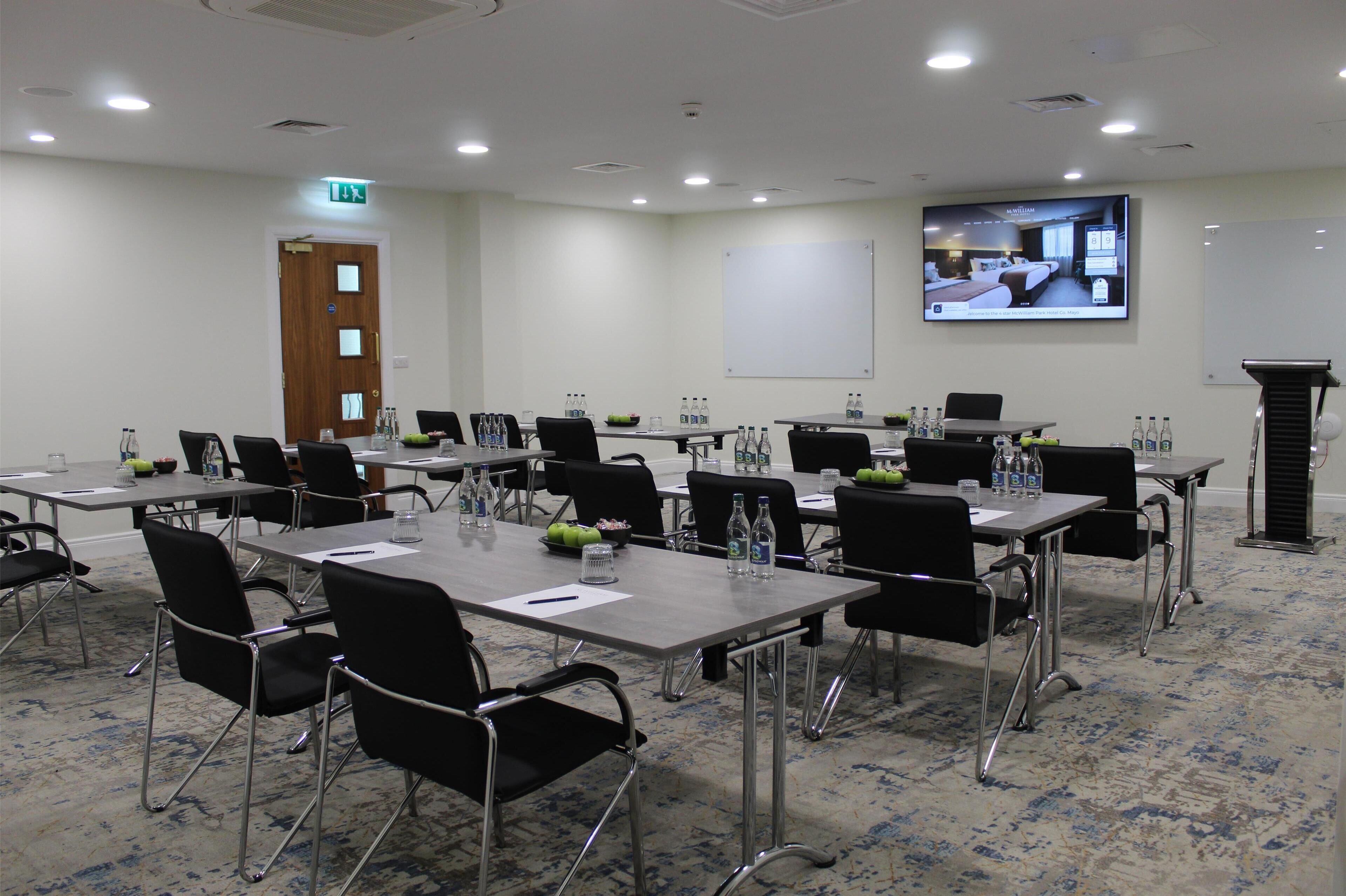 A conference room with tables, chairs, and a large screen displaying a hotel room.