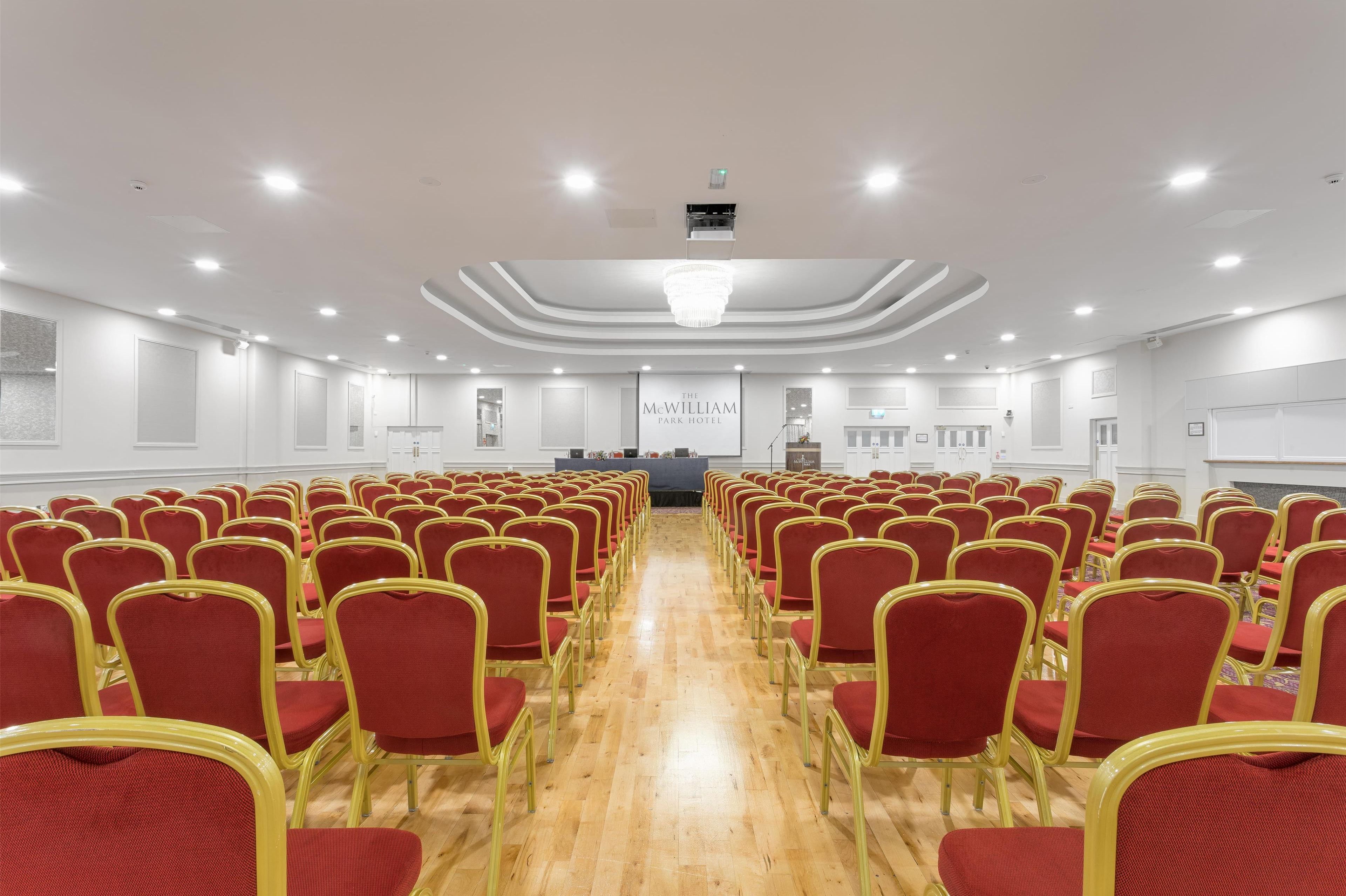 Una sala de conferències amb files de cadires vermelles i un escenari al capdamunt.