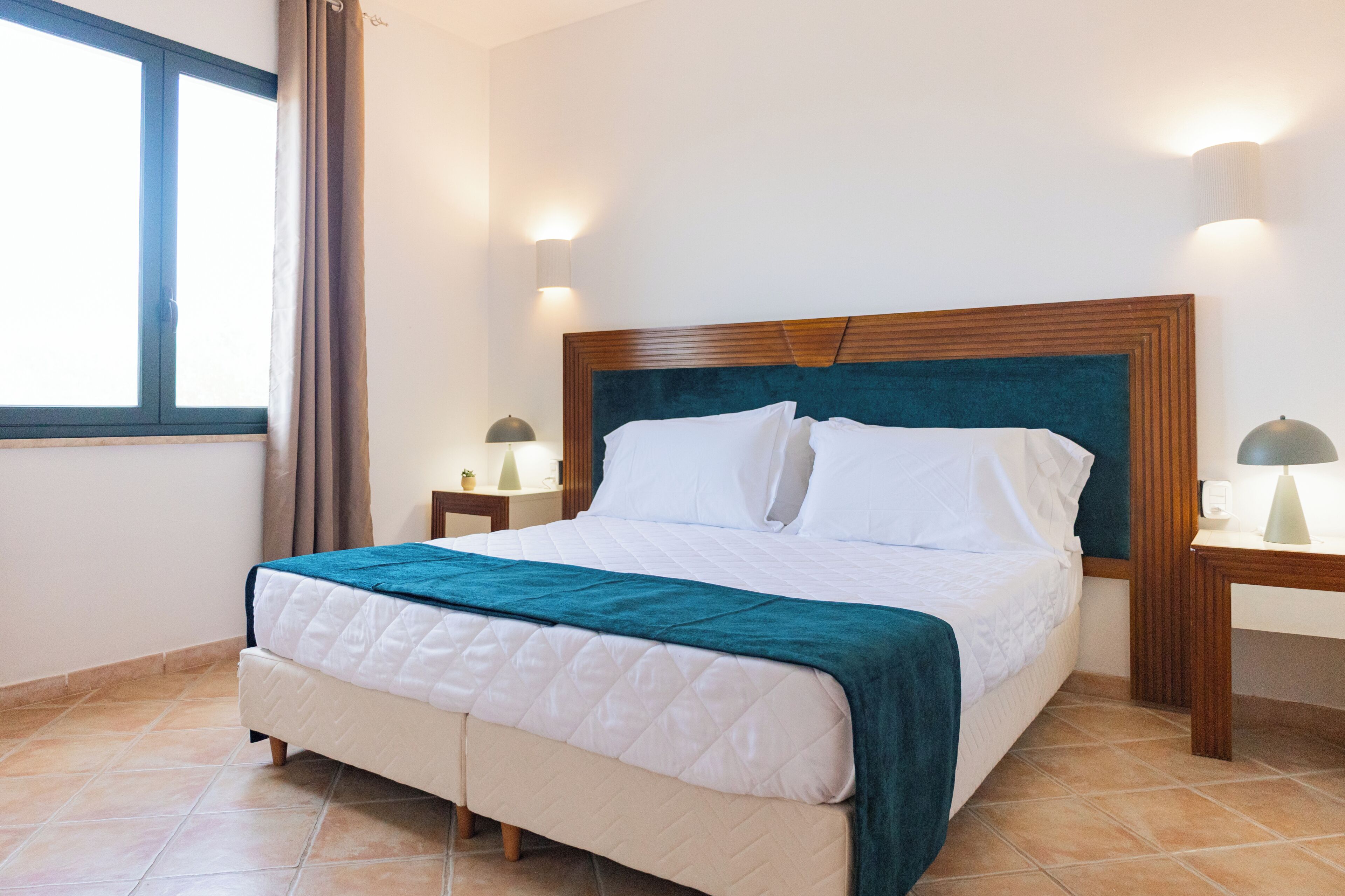 Ein Hotelzimmer mit einem Bett, zwei Nachttischen, einem mit Vorhängen versehenen Fenster und Wandlampen.