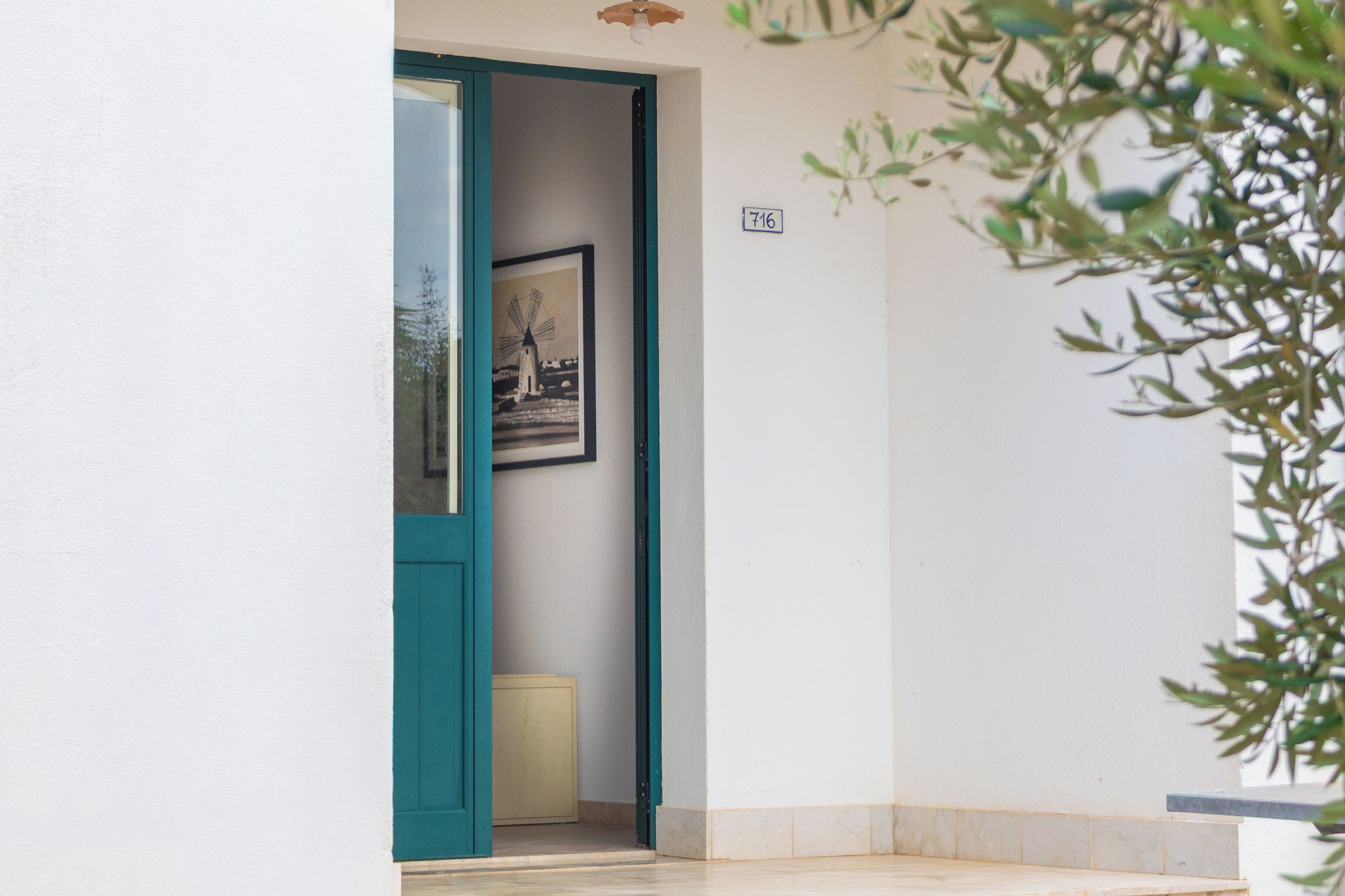 Una porta con cornice color petrolio, un quadro appeso alla parete e una piccola targa con il numero 716.