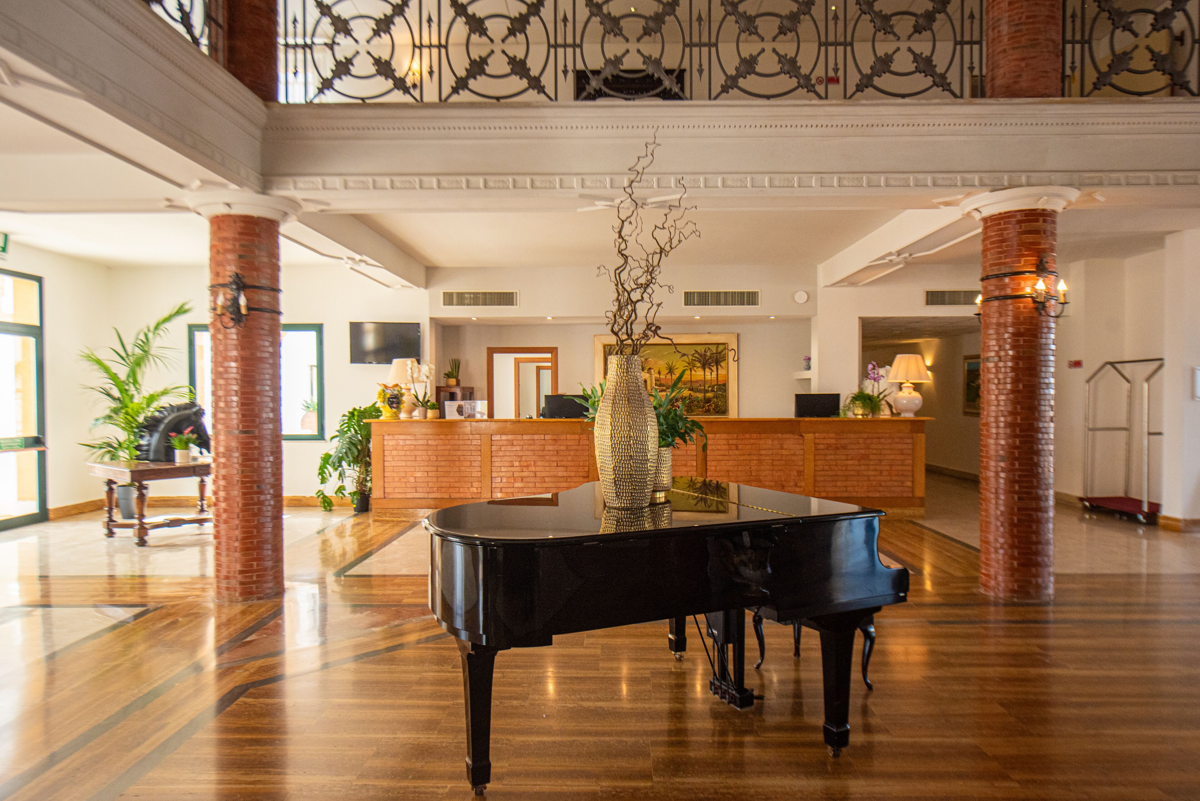 A grand lobby with a grand piano, a reception desk, and a high ceiling with decorative ironwork.