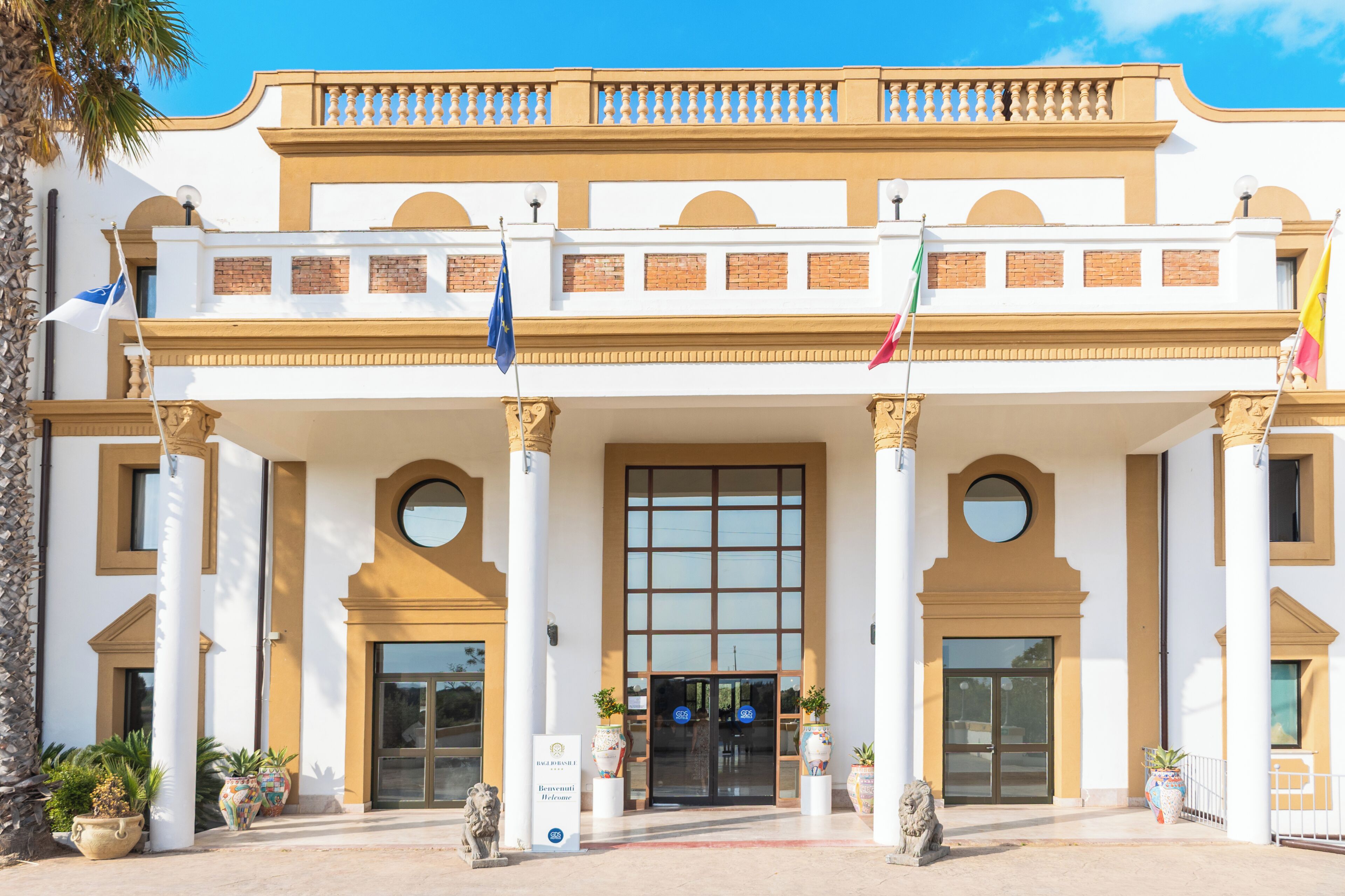 A hotel entrance with a large glass door, columns, and flags.