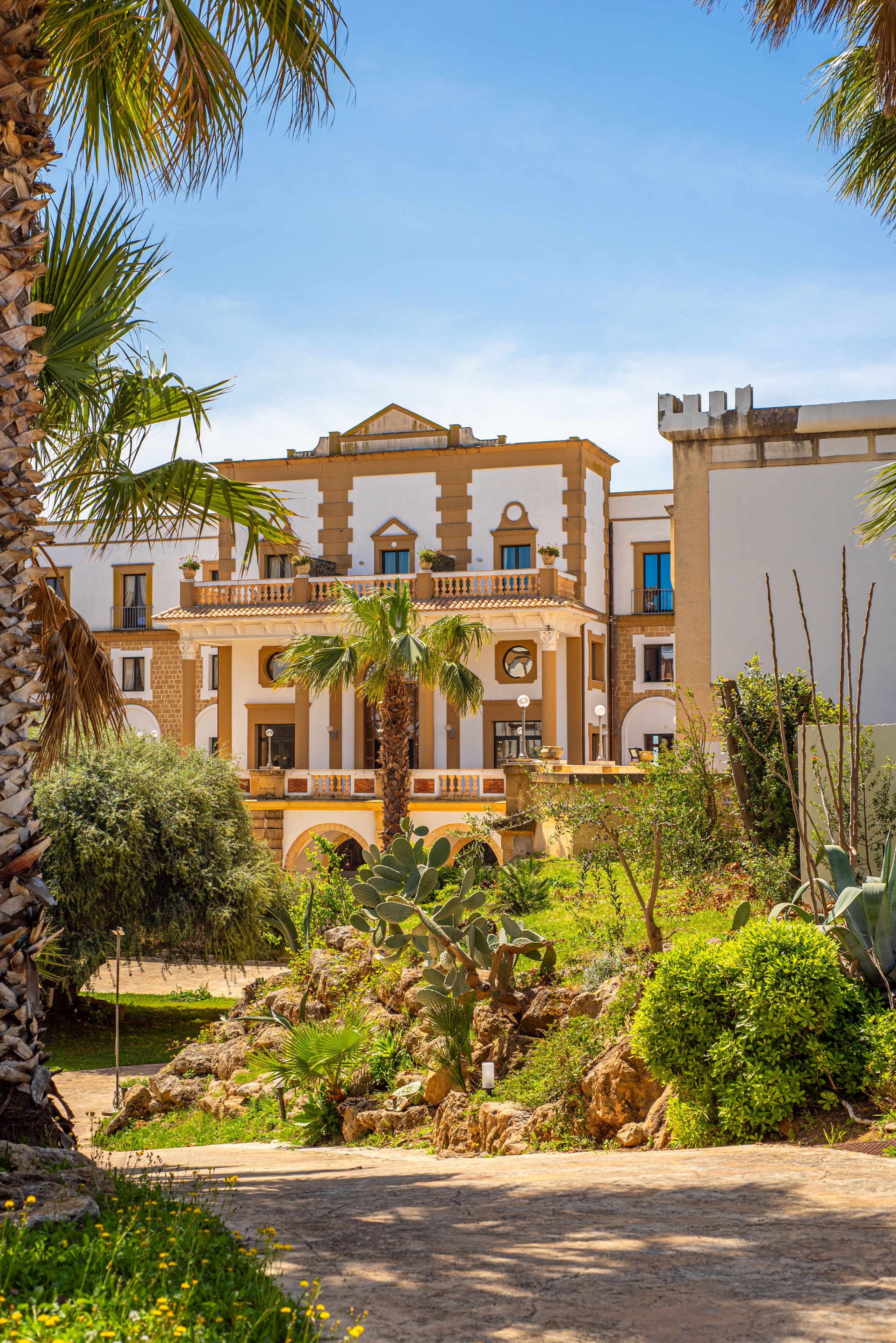 A building with a traditional architectural style, featuring a central courtyard with palm trees and cacti.