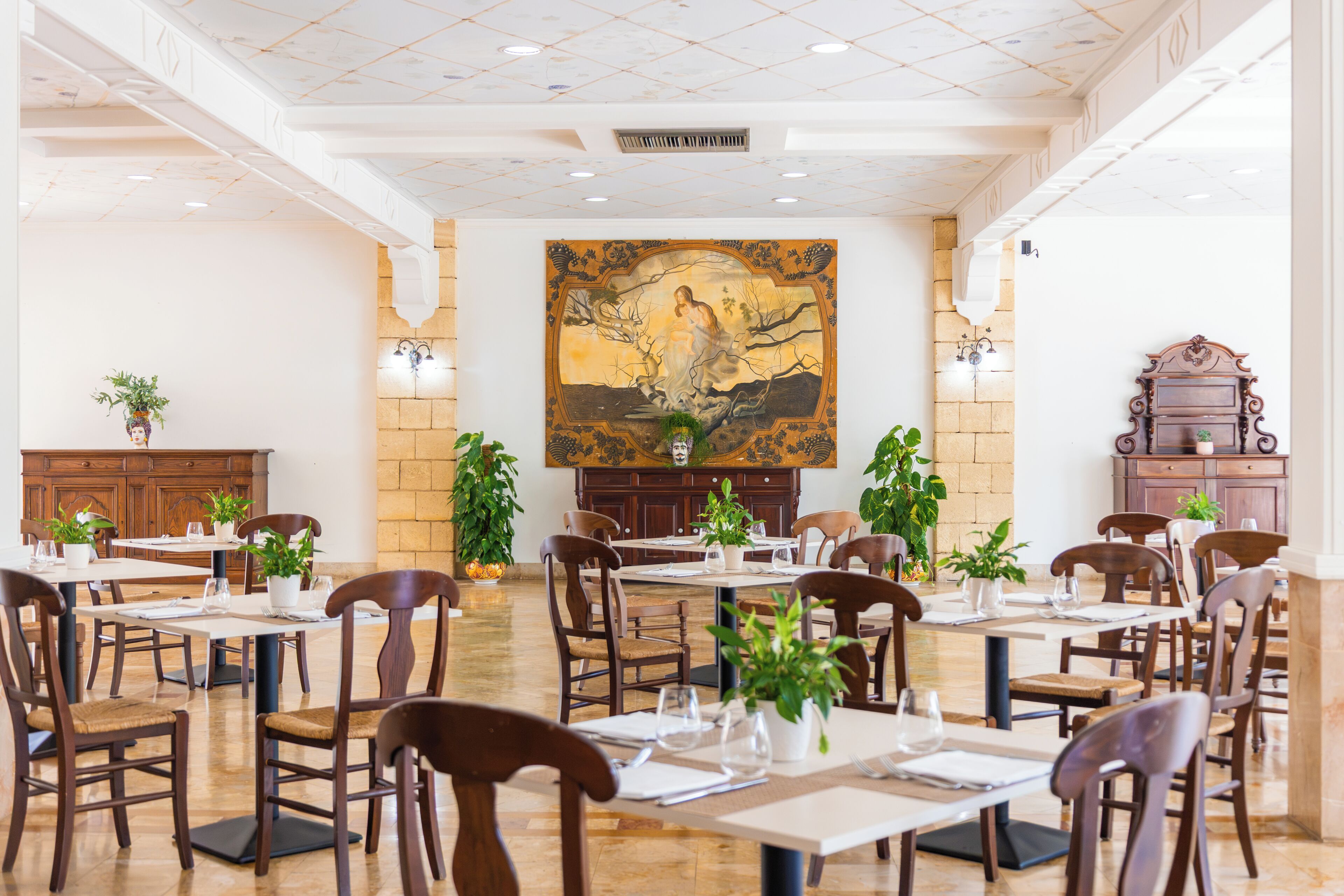 A spacious dining area with multiple tables and chairs, a large mural on the wall, and a brick wall.