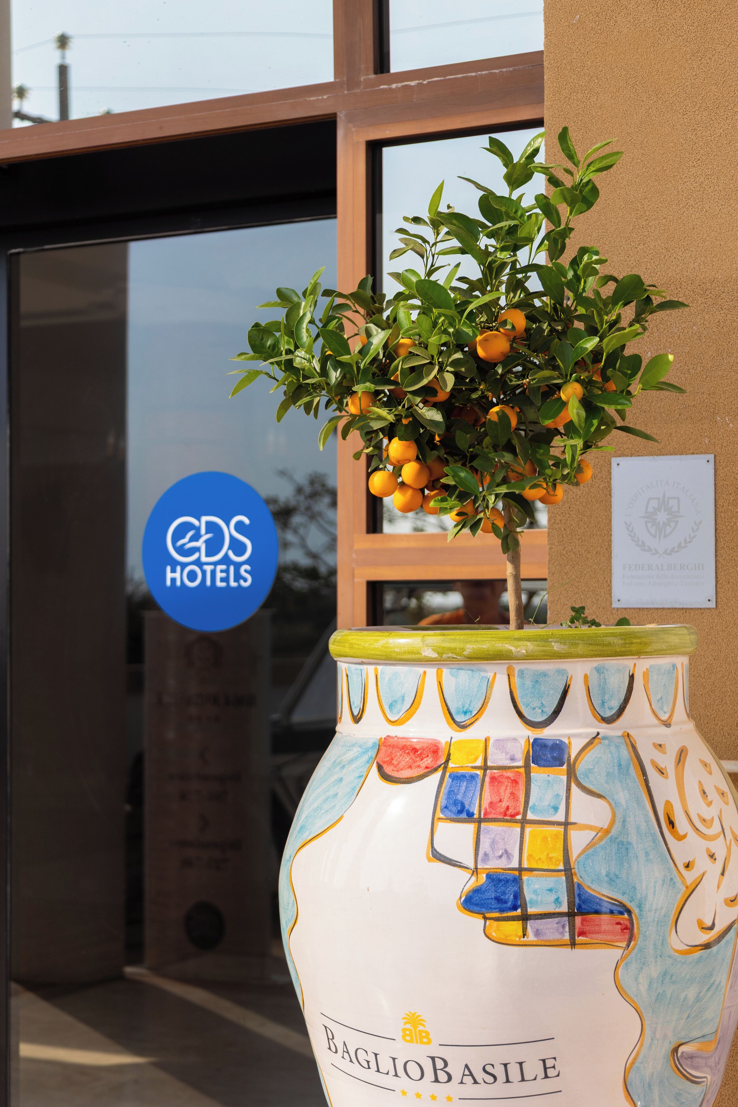 Un vase décoratif aux motifs colorés, placé à l’extérieur d’un bâtiment doté d’une porte en verre.