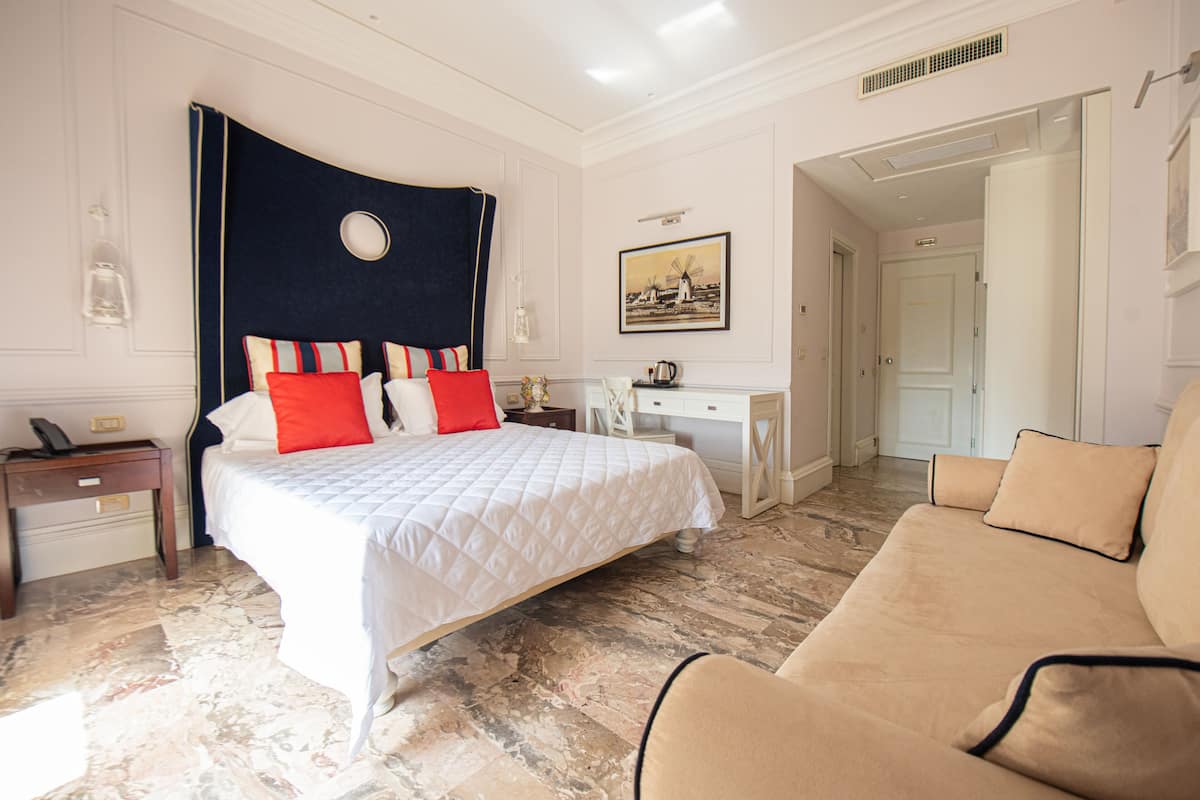 A hotel room with a bed, a desk, a chair, and a painting on the wall.