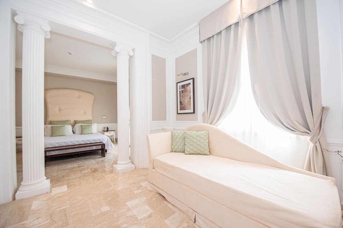 A bedroom with a bed, a sofa, a picture on the wall, and a window with curtains.