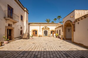 Un patio con pavimento de adoquines, un edificio central con una entrada arqueada y macetas con plantas.