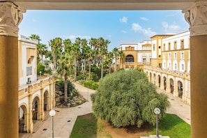 A courtyard with palm trees, a central bush, and classical architecture. - Baglio Basile Hotel (Petrosino)