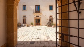 A courtyard with a building, a gate, and potted plants. - Baglio Basile Hotel (Petrosino)