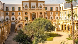 A courtyard with a central building featuring arches, a staircase, and a palm tree. - Baglio Basile Hotel (Petrosino)