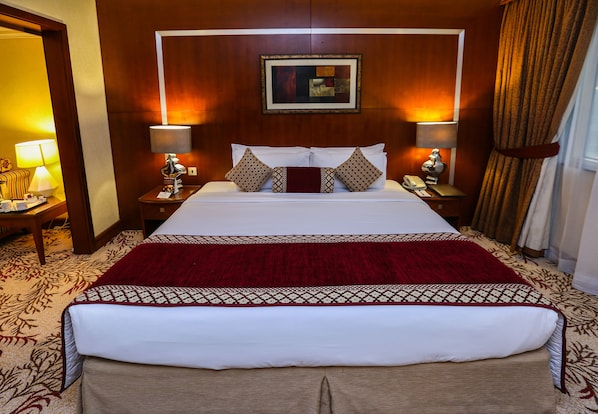 A hotel room with a large bed, two bedside tables with lamps, a red throw blanket, and a framed picture on the wall.