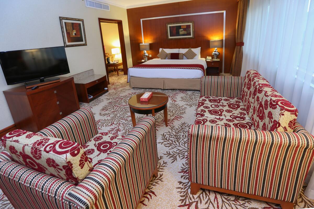 Una habitación de hotel con una cama, televisión, sofá, mesa de centro y alfombra estampada.