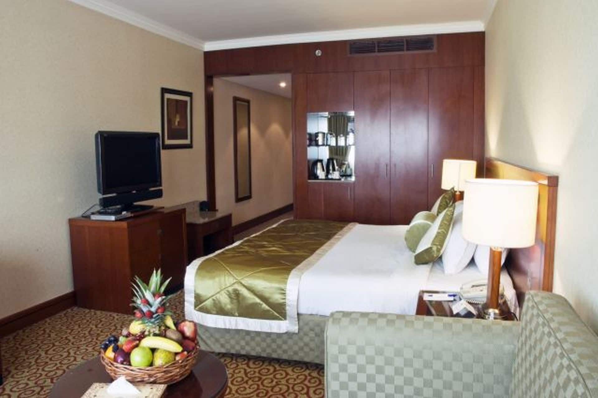 A hotel room with a bed, a television, a desk, a chair, a lamp, and a fruit basket.
