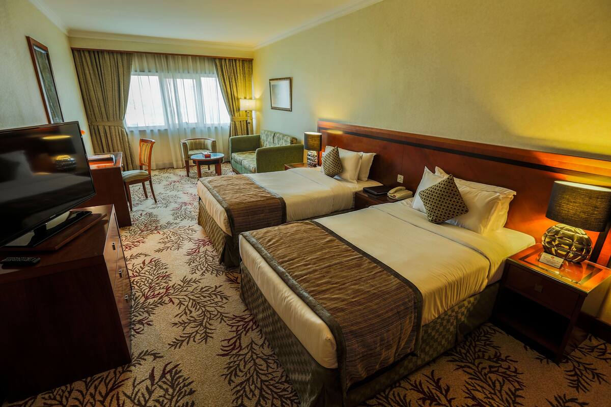 Habitación de hotel con dos camas, un escritorio con televisión, una silla y una mesita.
