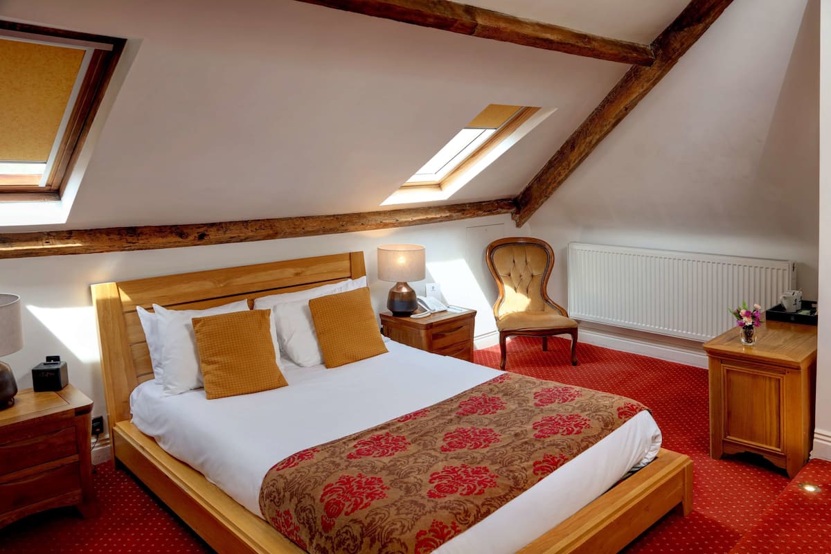 Een slaapkamer met een houten bed, een rode vloerkleed, een nachtkastje van hout, een stoel en een bureau met een lamp.