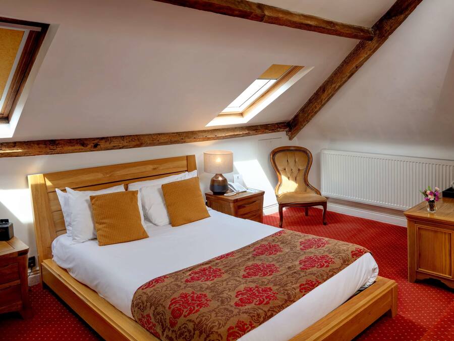 A bedroom with a wooden bed, a red carpet, a wooden nightstand, a chair, and a desk with a lamp.