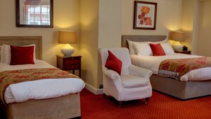 Habitación de hotel con dos camas, una silla y dos mesitas de noche con lámparas.