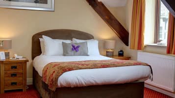 A neatly made bed with a headboard, two bedside tables with lamps, a framed picture on the wall, and a window with curtains.