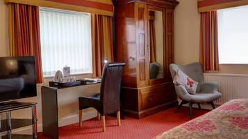 A hotel room with a wooden wardrobe, a desk with a chair, a television, and a bed with a floral bedspread.