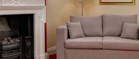A living room with a beige sofa, a fireplace, a red patterned carpet, and a floor lamp.