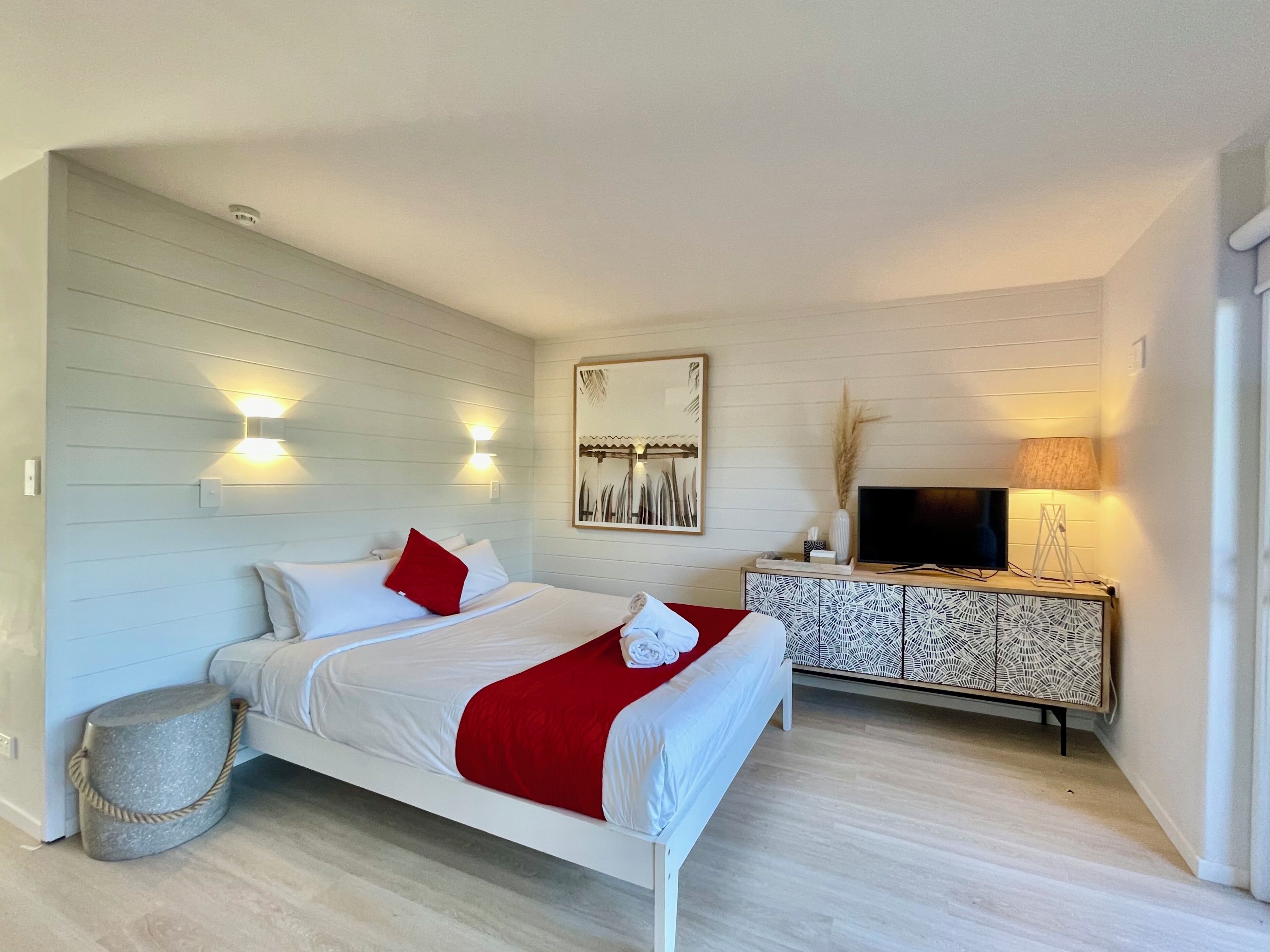 A modern bedroom with a bed, bedside lamps, a TV, and a decorative cabinet.