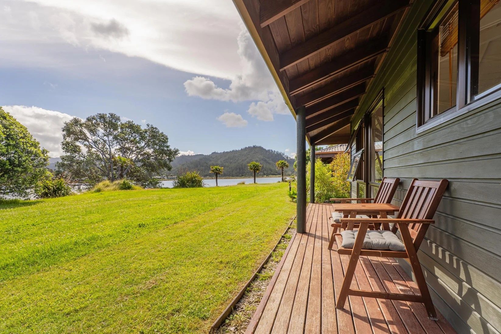 A wooden deck with outdoor seating, a grassy lawn, and a view of a lake and mountains.