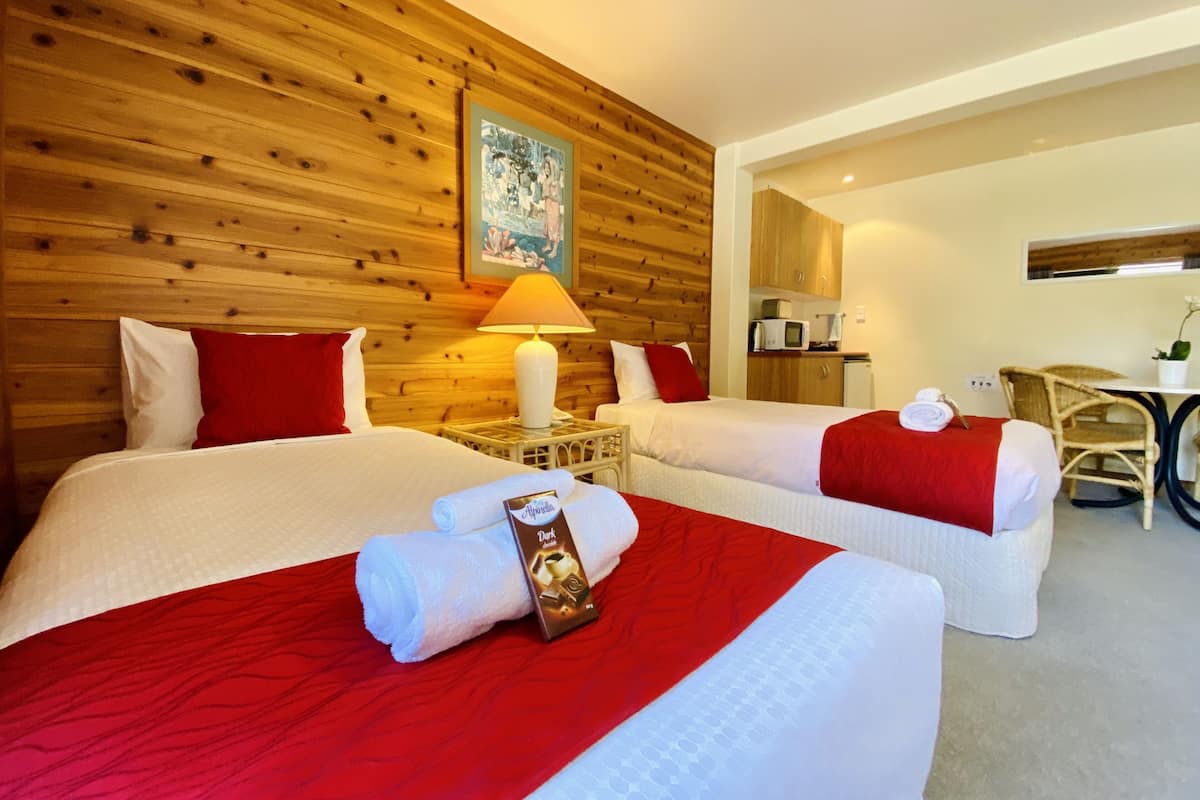 Ein Hotelzimmer mit zwei Betten, Holzvertäfelung an den Wänden, einem Gemälde, einem Schreibtisch mit Stuhl und einer kleinen Küchenzeile.