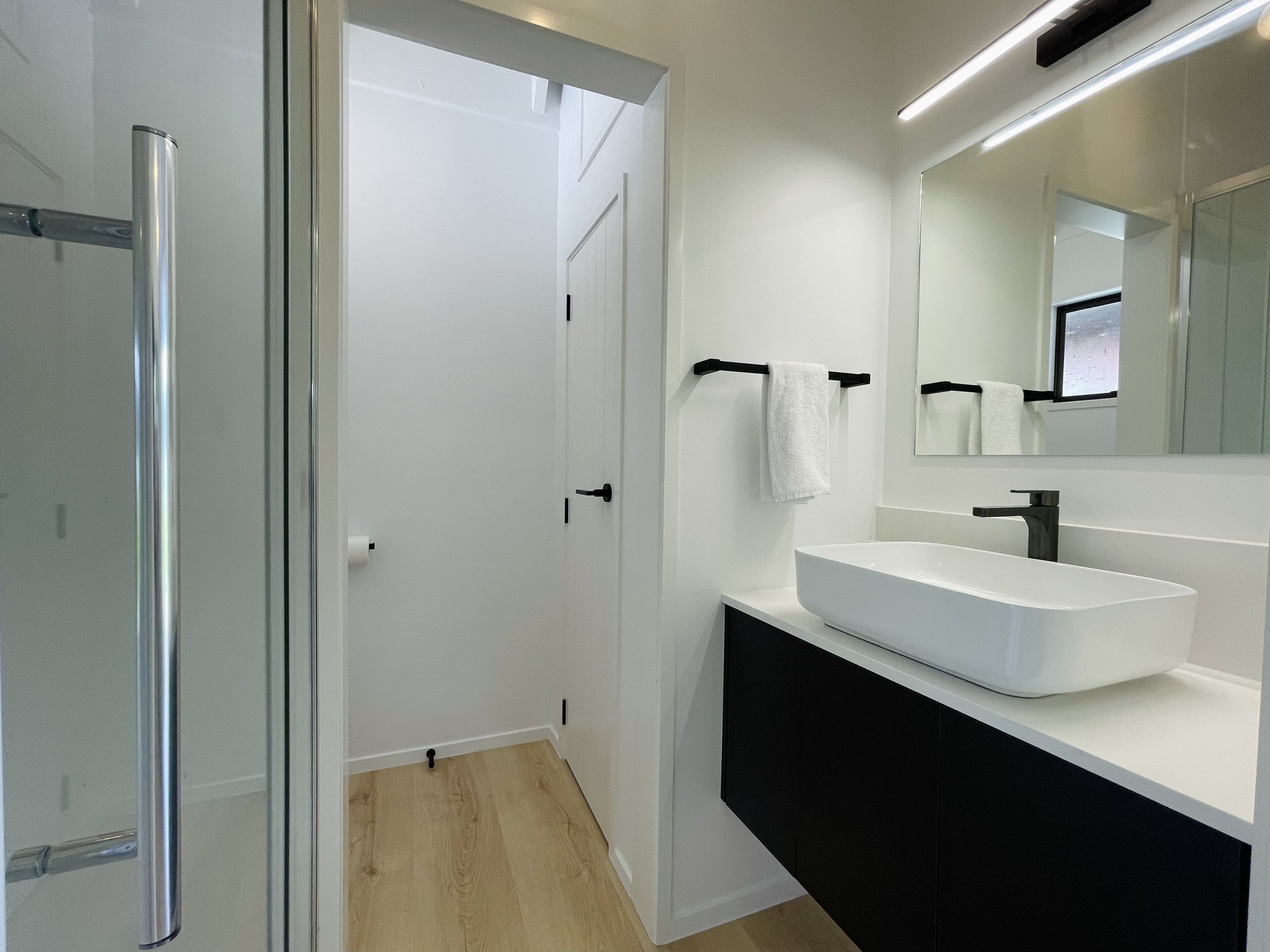 A modern bathroom with a glass shower enclosure, a white sink, and a black vanity.