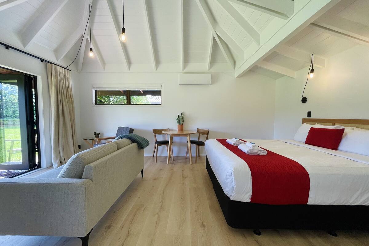 Ein modernes Hotelzimmer mit einem großen Bett, einer Couch, einem Esstisch und Blick ins Freie.