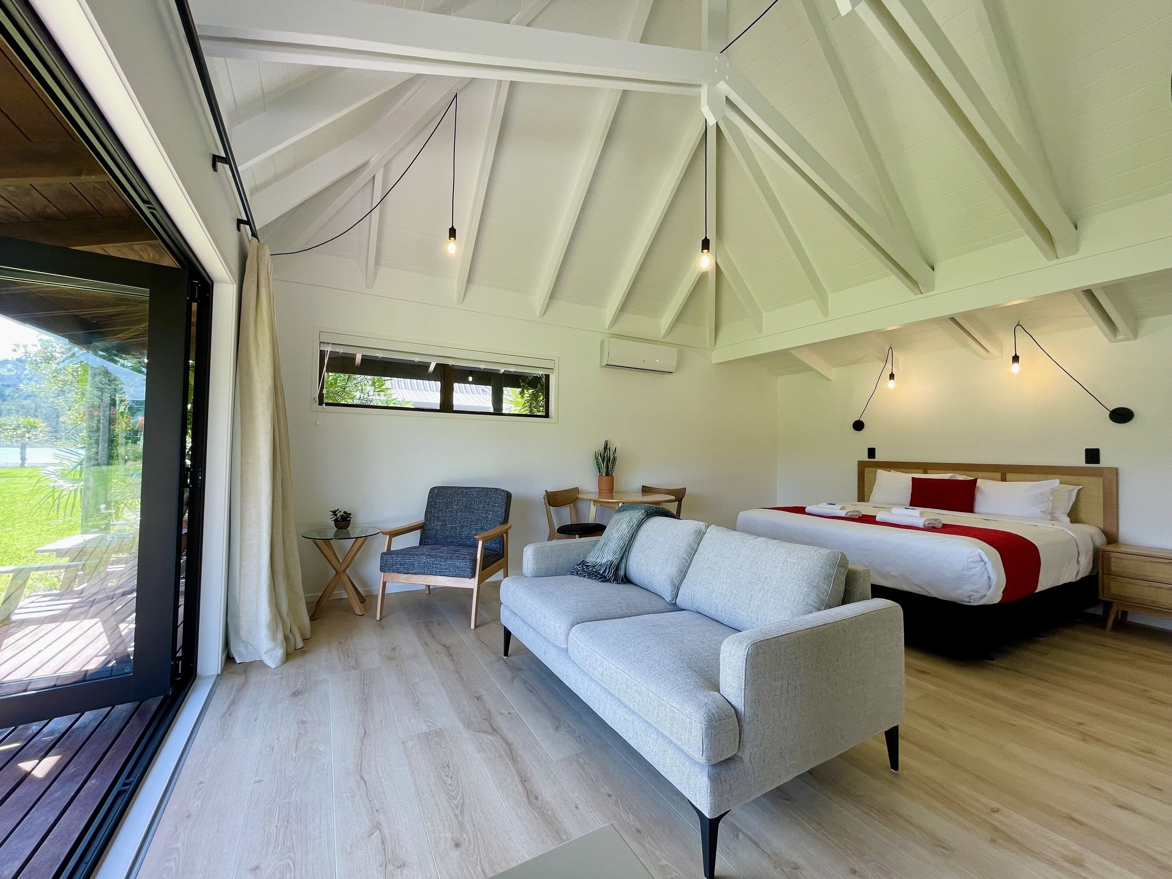 A spacious room with a large bed, a sofa, a chair, and a small table. There is a window with a view of greenery outside.