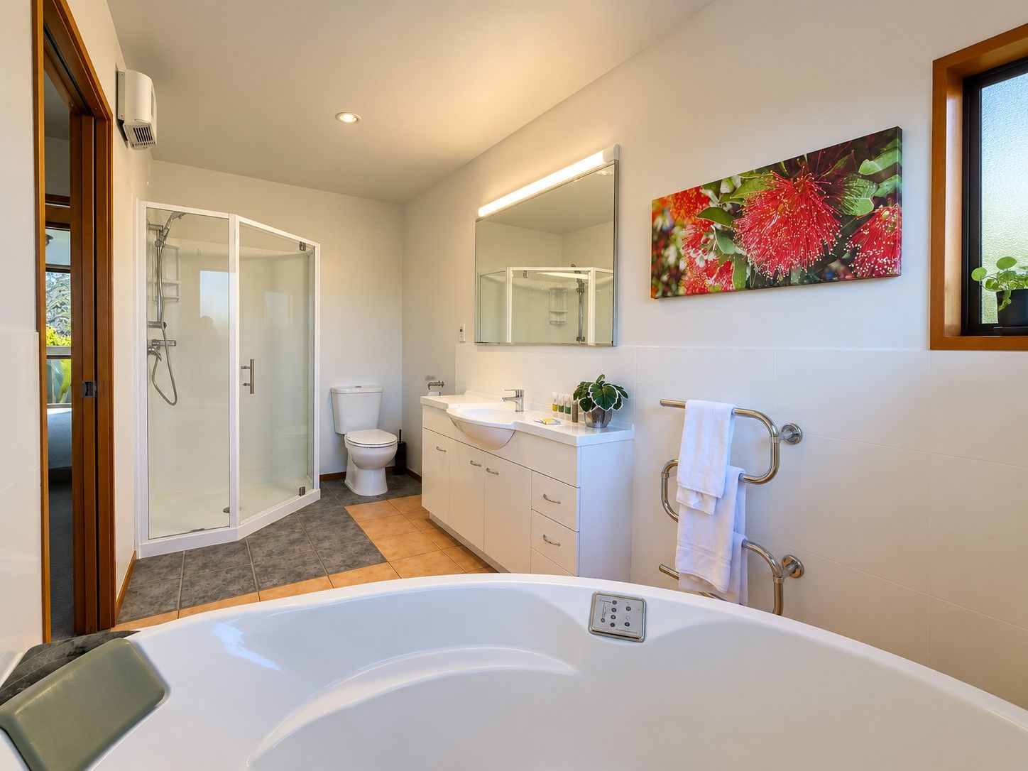Et stilfuldt badeværelse med bruseniche, toilet, vask med spejl og et badekar.