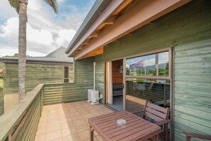 Eine Holzterrasse mit Tisch und Stühlen, eine Schiebeglastür, die zu einer überdachten Terrasse führt, und Blick auf ein Gebirge.