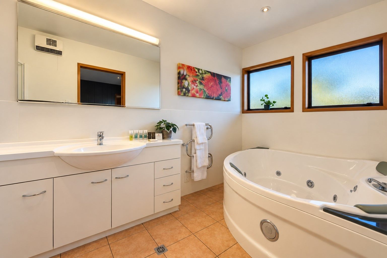 A modern bathroom with a large bathtub, a sink with toiletries, a mirror, and a window with a view.