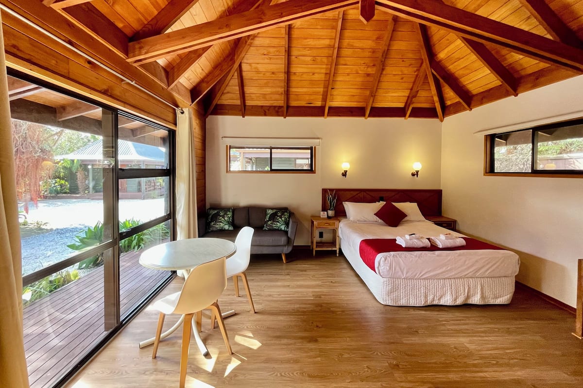 Ein geräumiges Zimmer mit einem großen Bett, einem Esstisch mit Stühlen und Blick ins Freie durch eine Schiebetür.