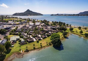 Vista aérea de una zona residencial costera con casas, un pequeño lago y una colina distante.