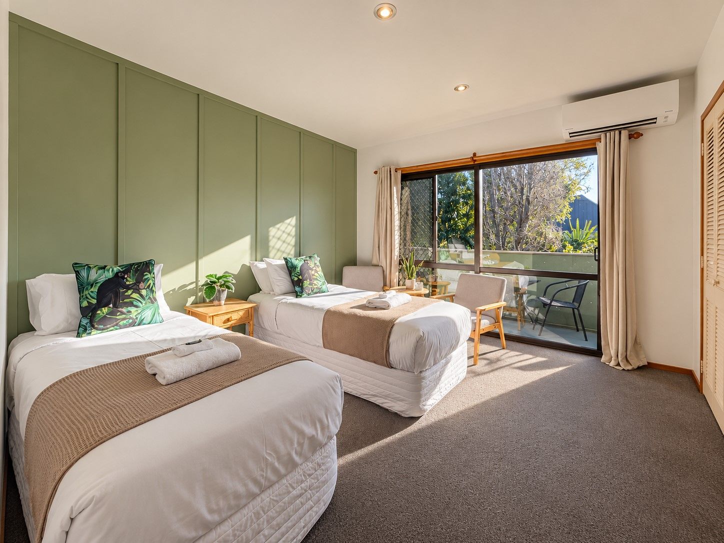 A hotel room with two beds, a desk, a chair, and a balcony with a view.