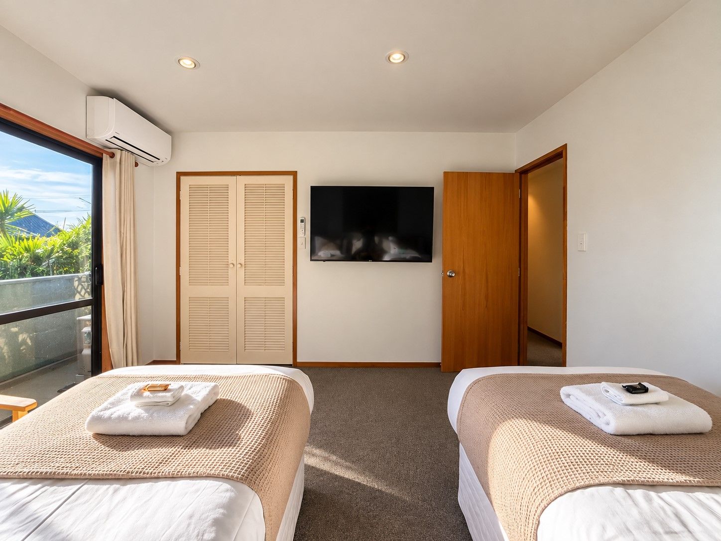 A hotel room with two beds, a TV, a wardrobe, and a balcony with a view.