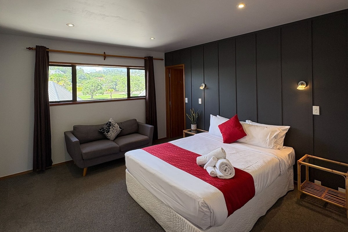 Ein modernes Hotelzimmer mit einem großen Bett, einer Sitzecke und Blick auf Grün.