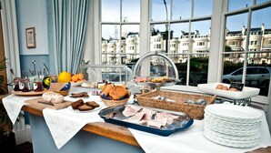 Ein Frühstücksbuffet mit verschiedenen Speisen und Blick auf die Stadt durch große Fenster.