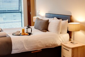 A neatly made bed with pillows, a bedside table with a lamp, and a tray with breakfast items. - Base Serviced Apartments - Duke Street (Liverpool)