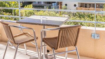 A balcony with a table and two wicker chairs, overlooking a building and greenery.