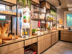 A breakfast bar with bread, pastries, and a juice dispenser. - Ibis Roquebrune Cap Martin Menton (Roquebrune-Cap-Martin)