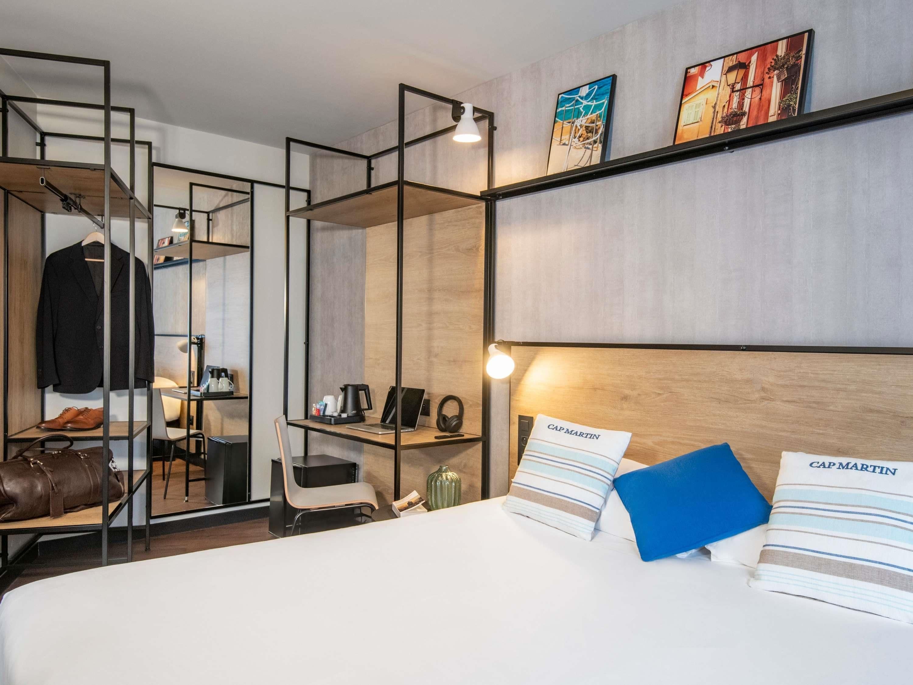 A hotel room with a bed, a desk, a chair, a coat rack, and a wardrobe.