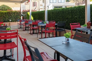 An outdoor cafe with tables and chairs, a hedge, and a building in the background. - Ibis Roquebrune Cap Martin Menton (Roquebrune-Cap-Martin)