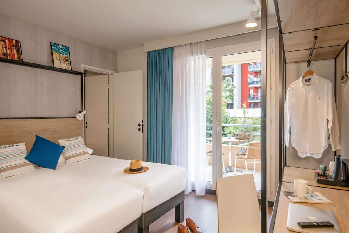 Une chambre d’hôtel avec un lit, un bureau, une chaise, un ordinateur portable et un manteau accroché.